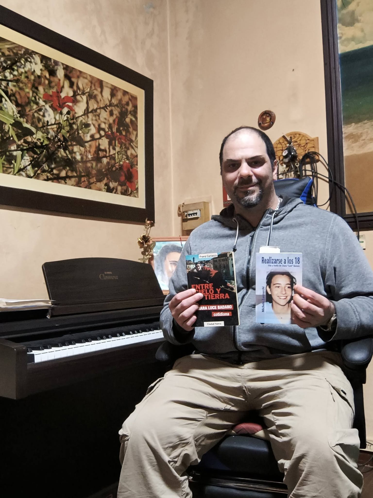Alejandro Gutiérrez junto a su piano sosteniendo libros sobre Chiara Luce Badano